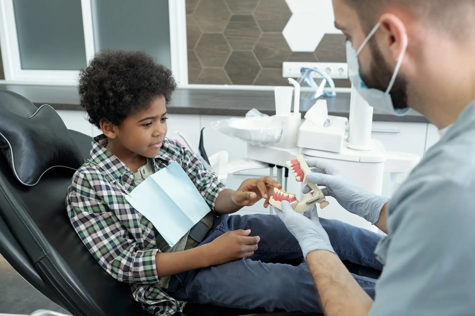 Curious little boy putting finger on lower teeth of false human jaws