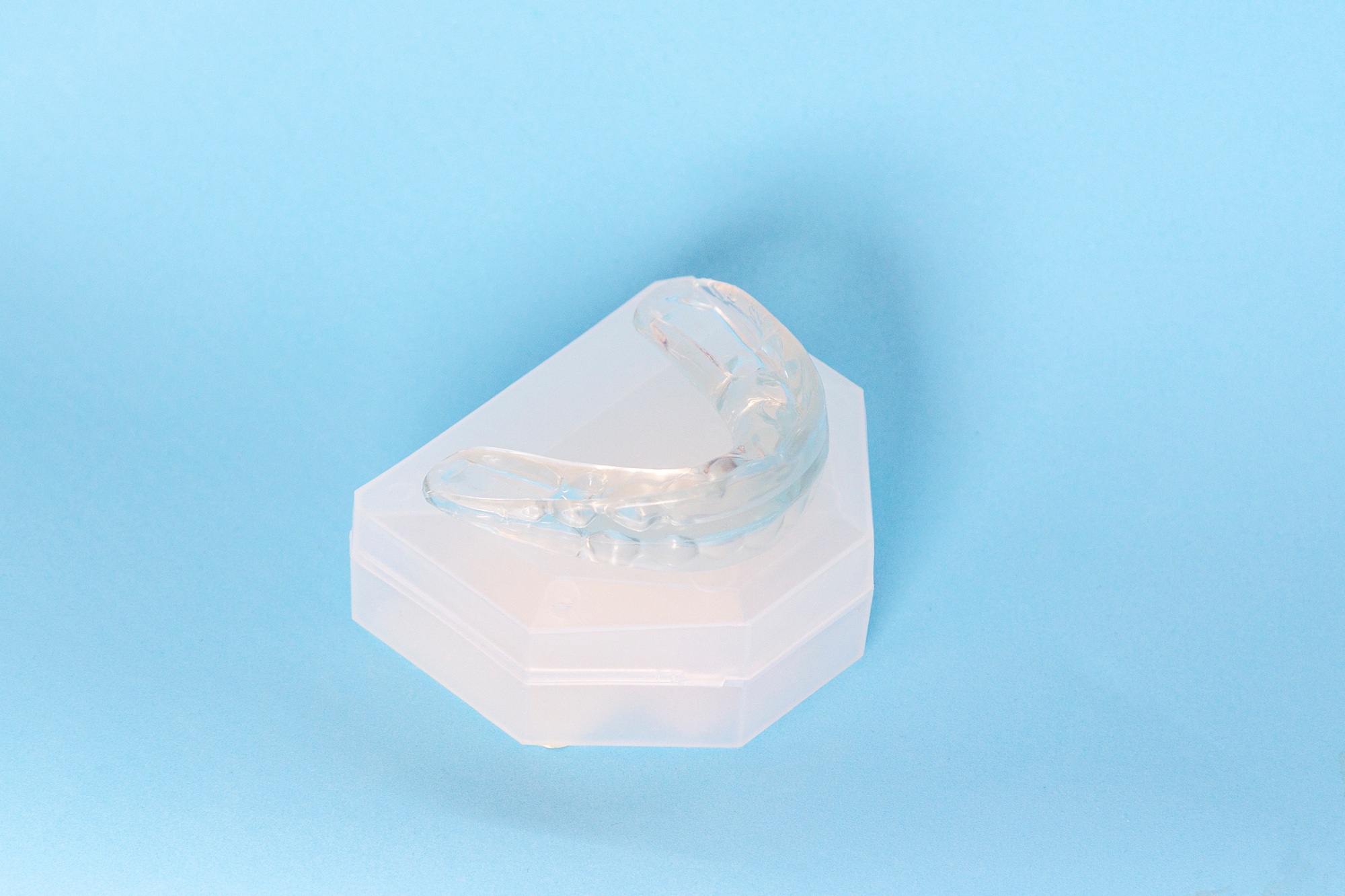 Silicone dental mouthguard, orthodontic trainer to correct bite on blue background