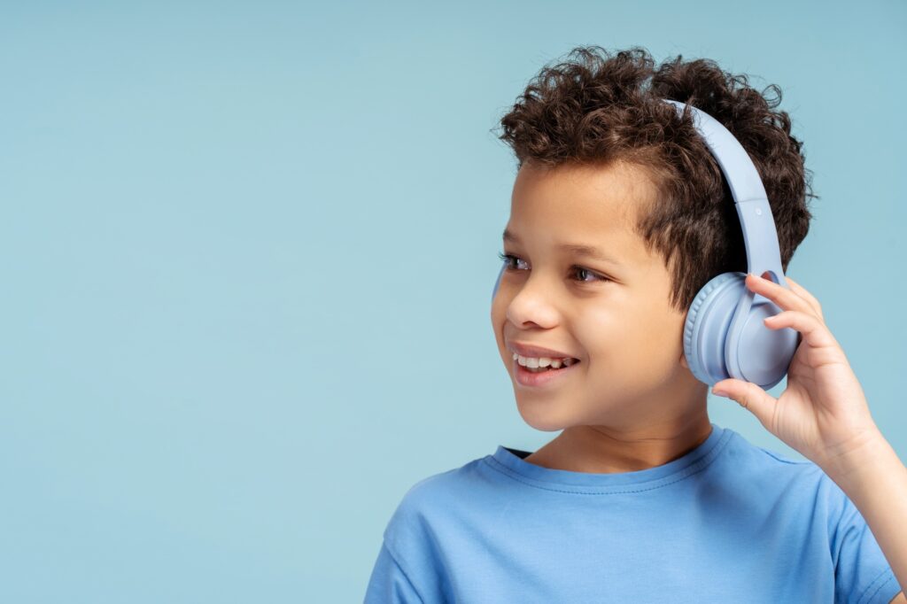 Smiling young African American boy, using wireless headphones, isolated on a solid blue background
